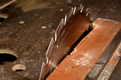 A close-up image of a circular saw blade on a table saw, surrounded by sawdust. The sharp metal teeth of the blade are partially embedded in a piece of wood, indicating it is in the process of cutting through the material. Personal injury attorneys often handle cases involving accidents with such tools.