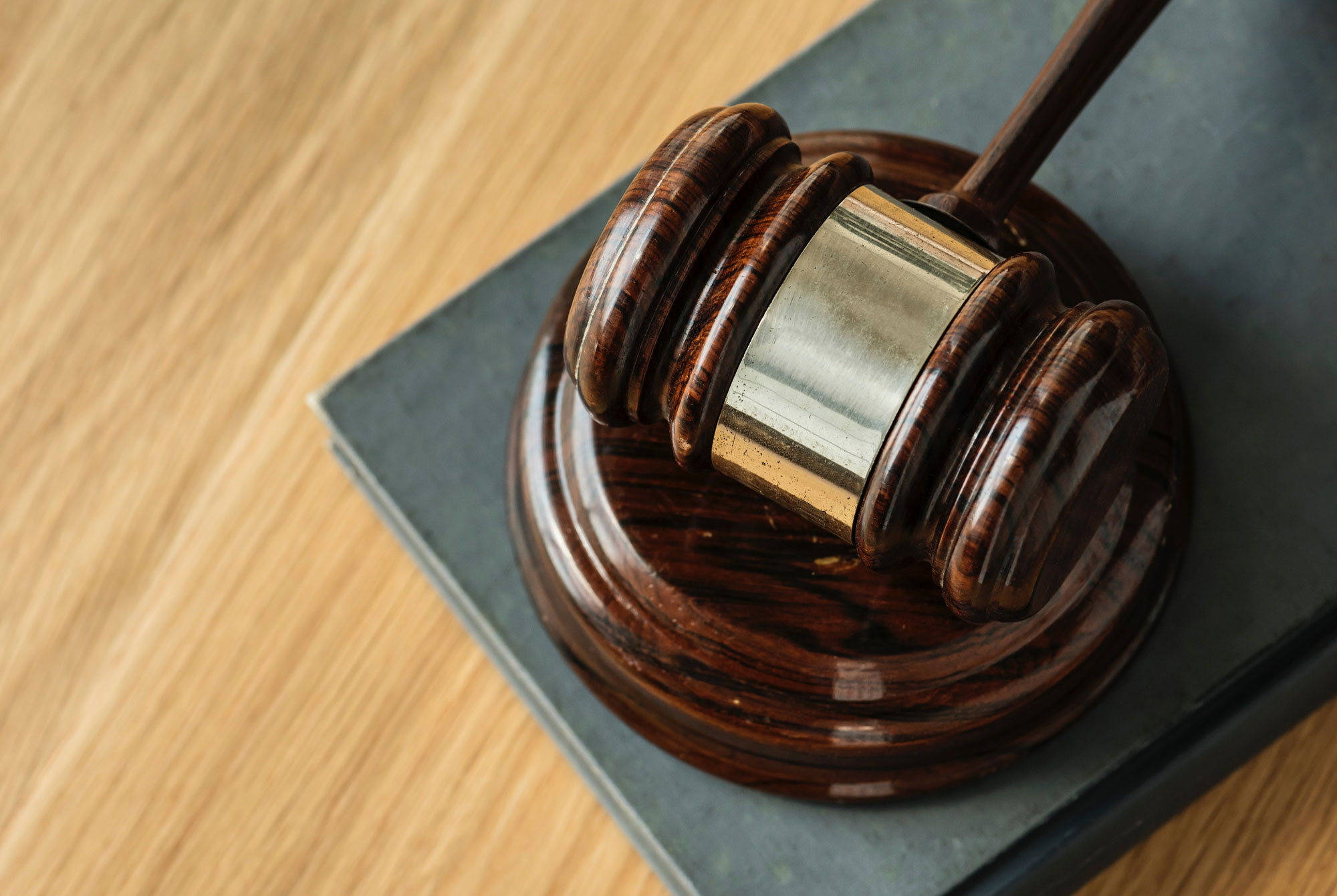 A close-up image of a dark wooden gavel resting on a block placed on a book. The gavel has a polished, smooth texture and metal band around its head. The background features a wooden surface, providing contrast to the gavel's darker wood—emblematic of personal injury attorneys' commitment to justice.