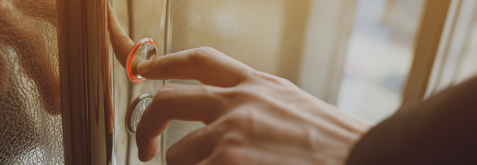 Close-up of a hand pressing a lit-up elevator button inside a modern elevator, as if seeking immediate assistance from injury lawyers. The button has a red glow indicating it has been activated. The background is softly blurred, focusing on the action of pressing the button.